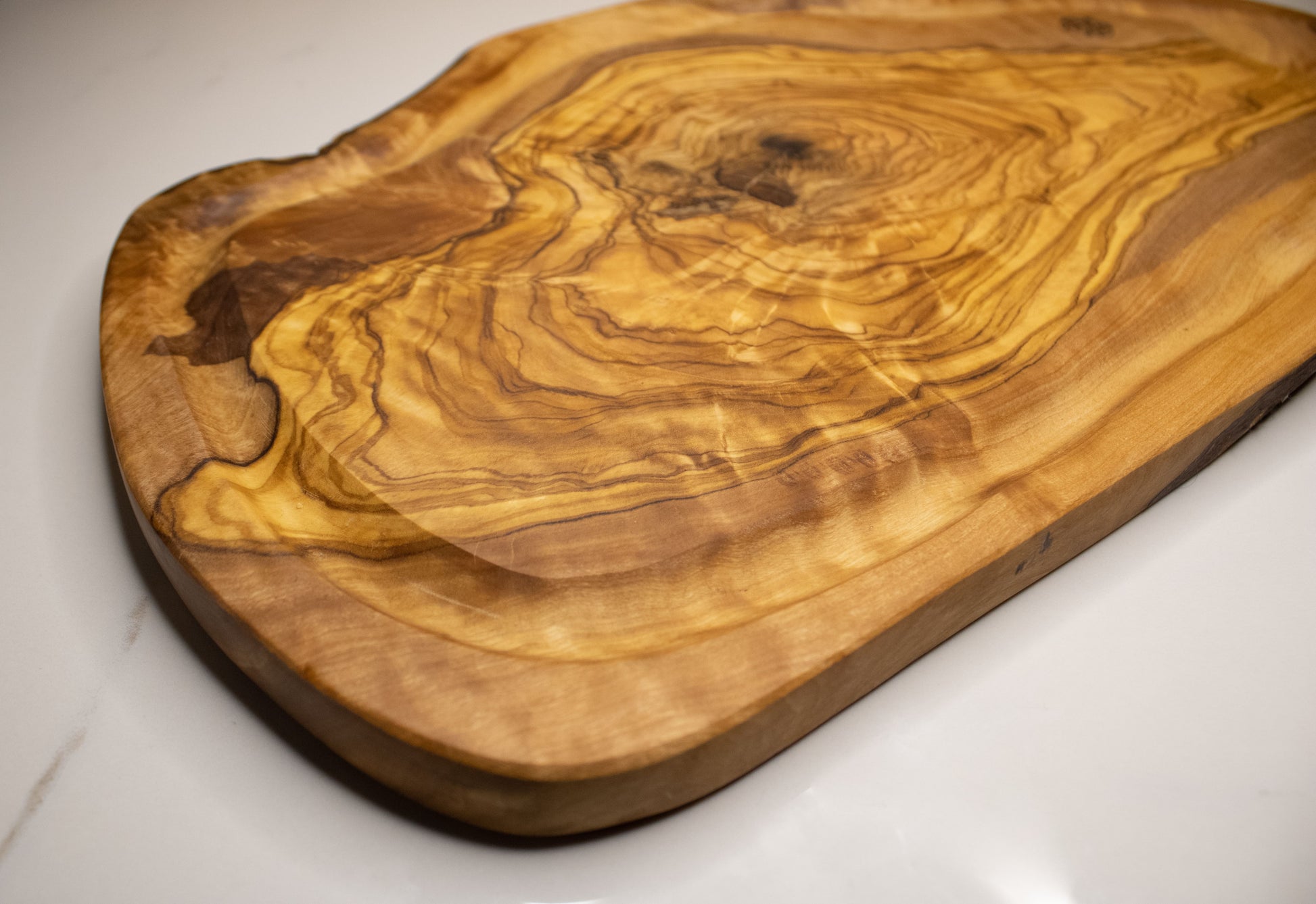 Planche avec rainures à jus en bois d&#39;olivier posé sur une table en marbre