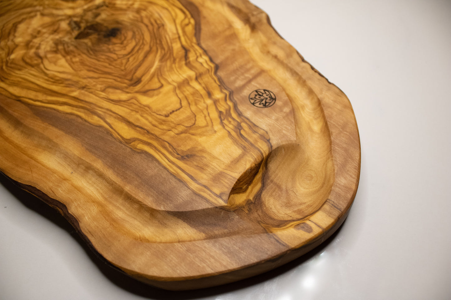 Planche avec rainures à jus en bois d&#39;olivier posé sur une table en marbre